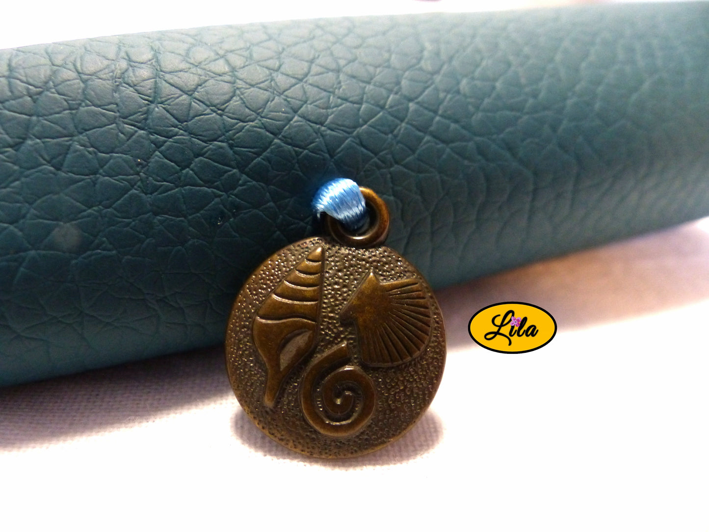 Zoom sur le pendentif pièce gravée aux motifs coquillage provenant d’un ancien bijou décorant l’étui à lunettes en simili turquoise détail bohème et vintage