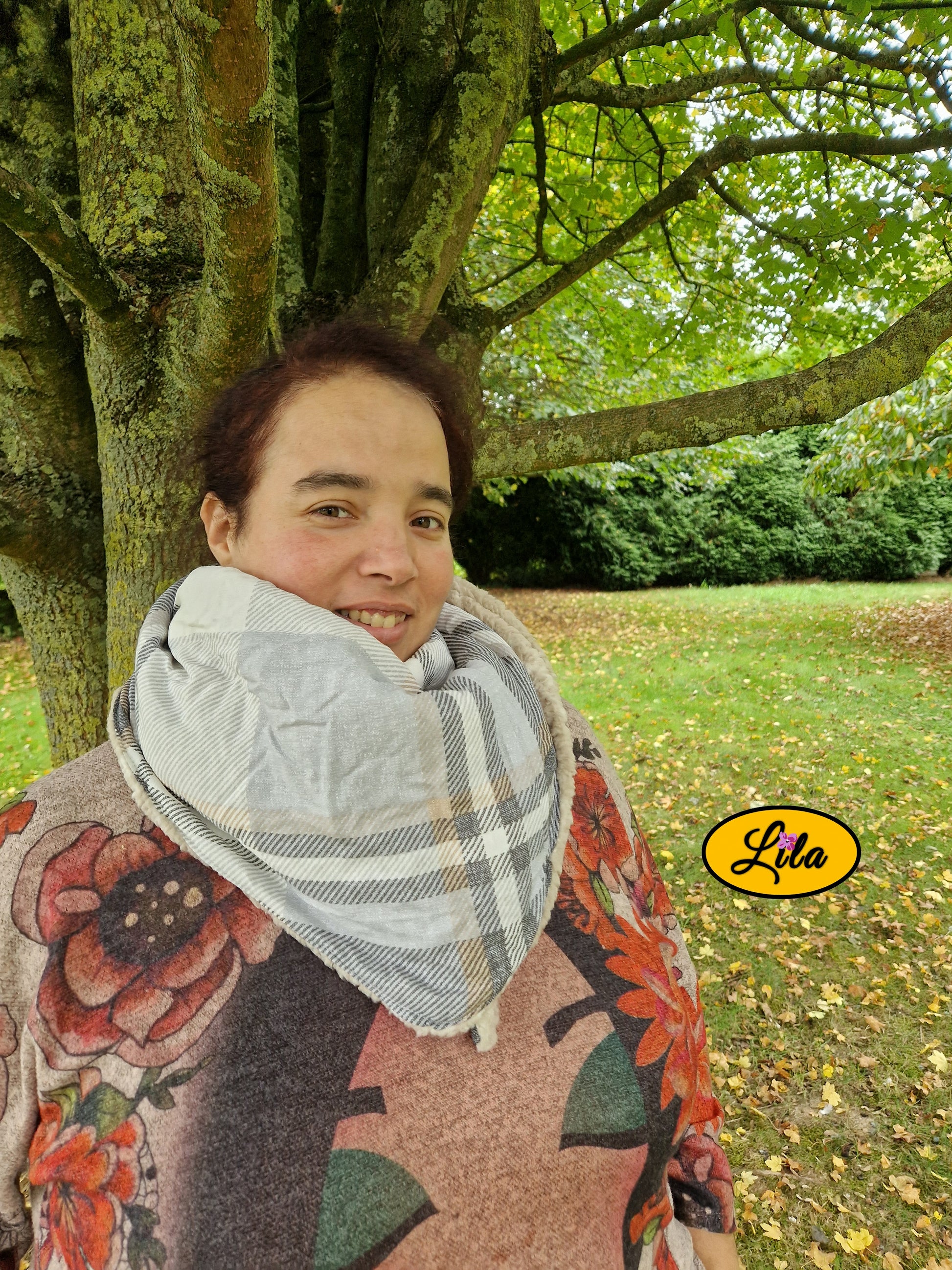 Foulard triangulaire en tartan brun porté fermé par une jeune fille appuyée contre un arbre avec nœud caché sous la pointe du foulard photo cadrée de plus près style rétro et hivernal