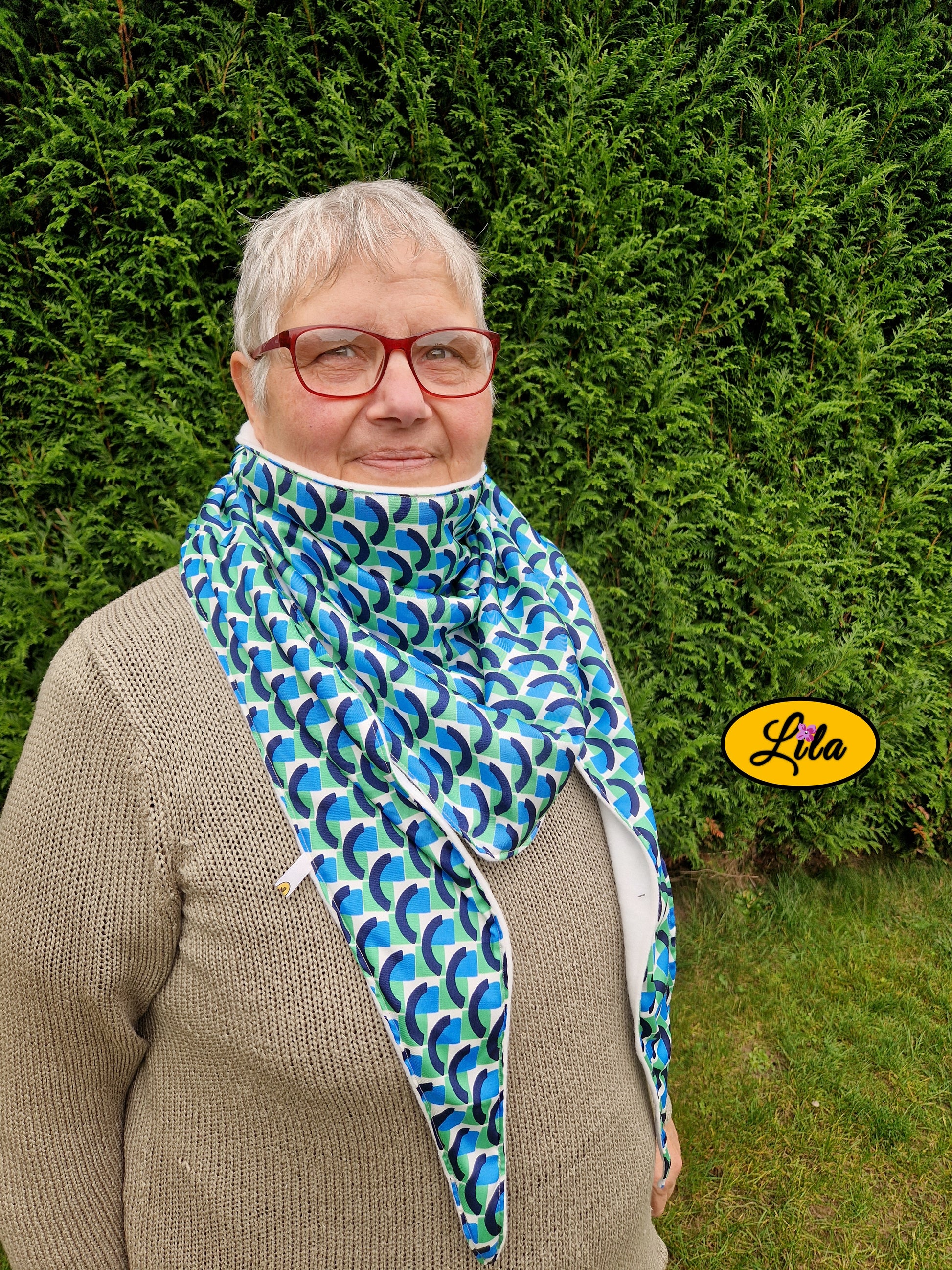 Foulard triangulaire esprit vintage vert bleu et blanc porté par une dame à lunettes dans un jardin profil droit regard tourné vers l’objectif style cocooning et rétro