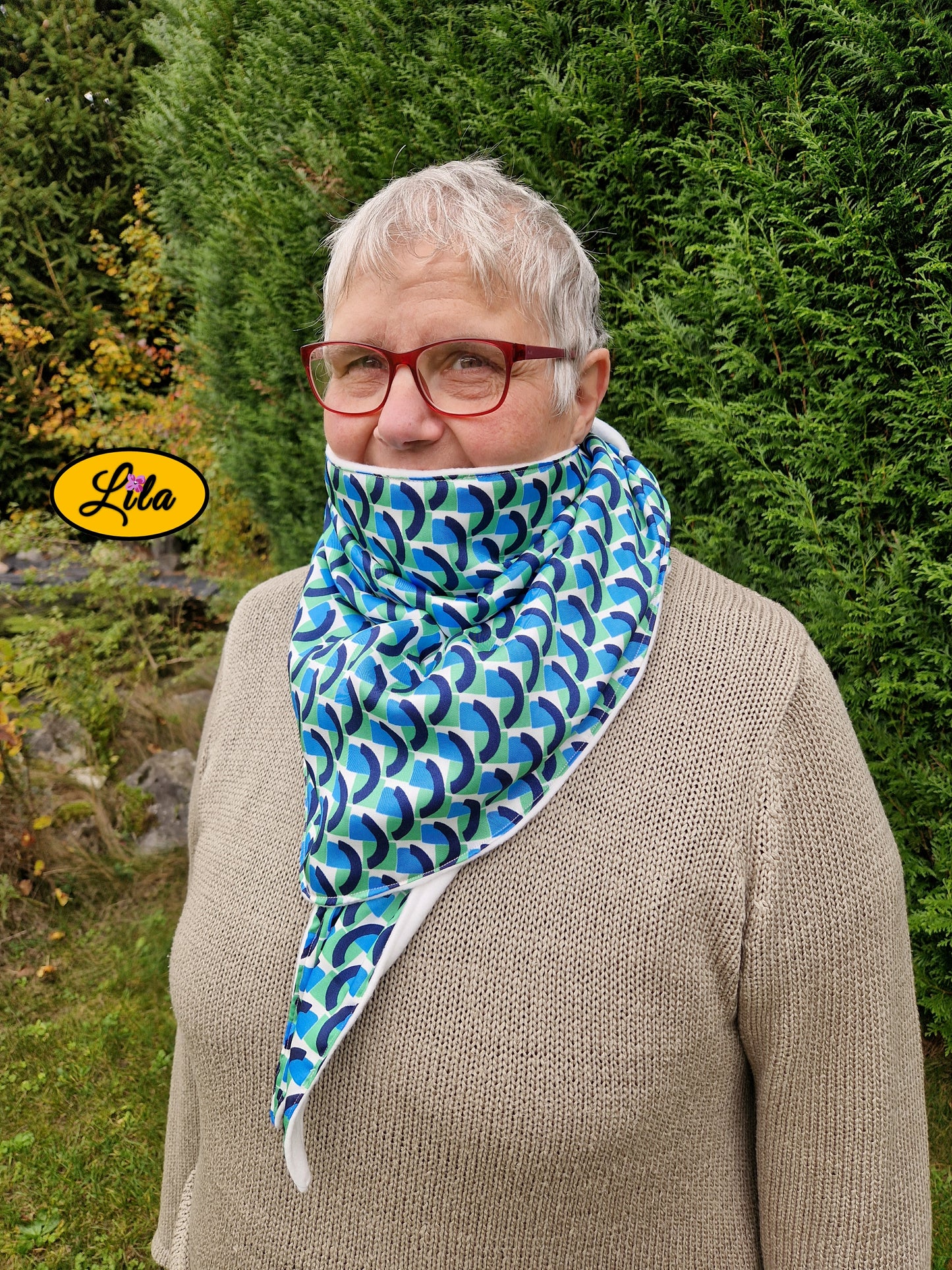 Foulard triangulaire esprit vintage vert bleu et blanc porté fermé par une dame à lunettes de profil gauche avec nœud caché sous la pointe du foulard et foulard remonté couvrant la bouche style hivernal et cocooning