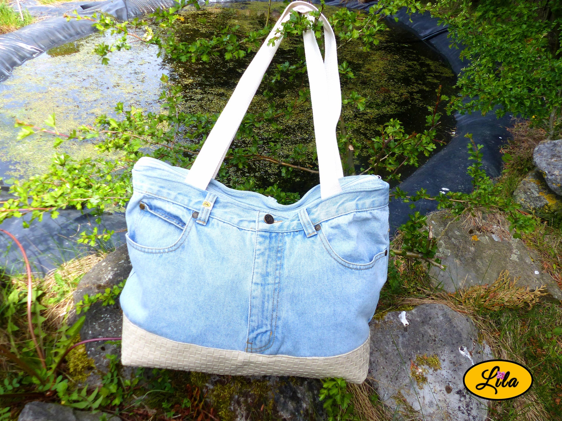 Grand sac en jeans clair recyclé et simili cuir crème posé devant un étang dans un décor naturel mettant en valeur son style élégant et écoresponsable