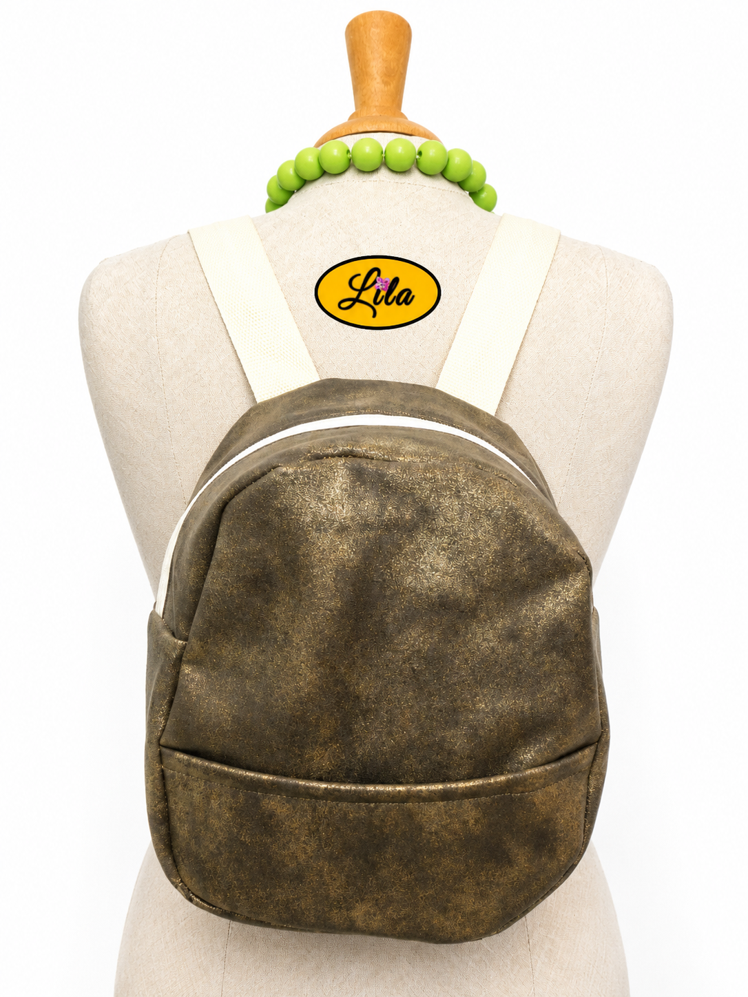 Mini sac à dos en simili brun doré avec poche avant et sangle crème porté sur mannequin de couture sur fond blanc style chic et moderne