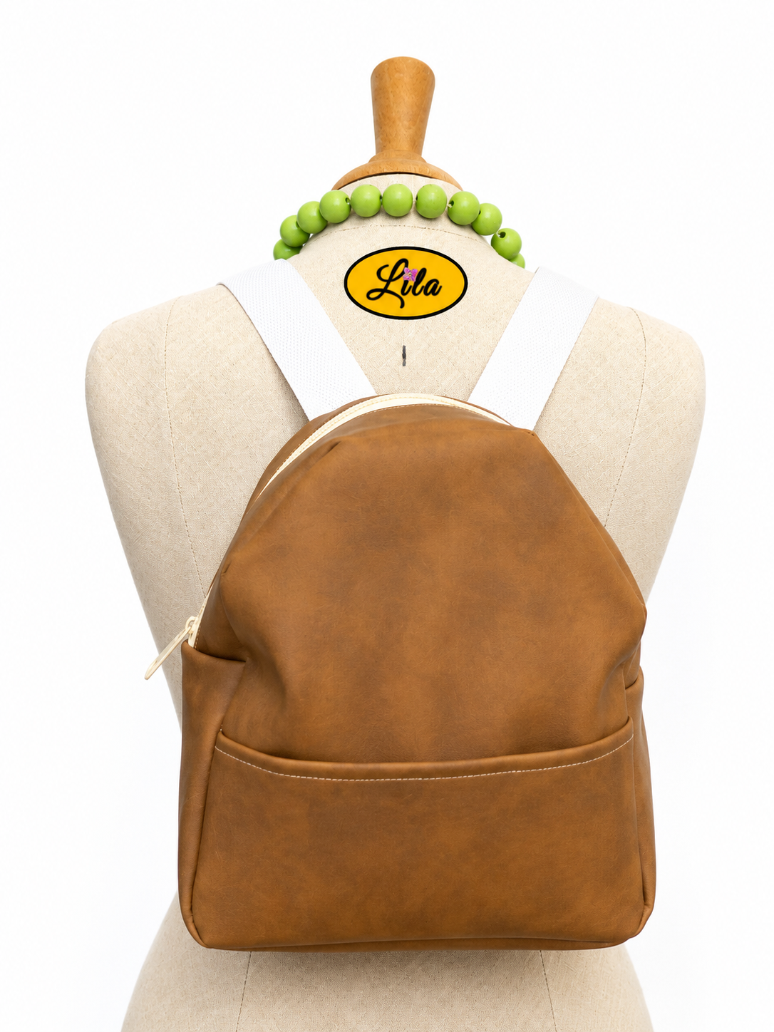 Mini sac à dos en simili brun avec poche avant et sangle blanche porté sur mannequin de couture sur fond blanc style élégant et moderne
