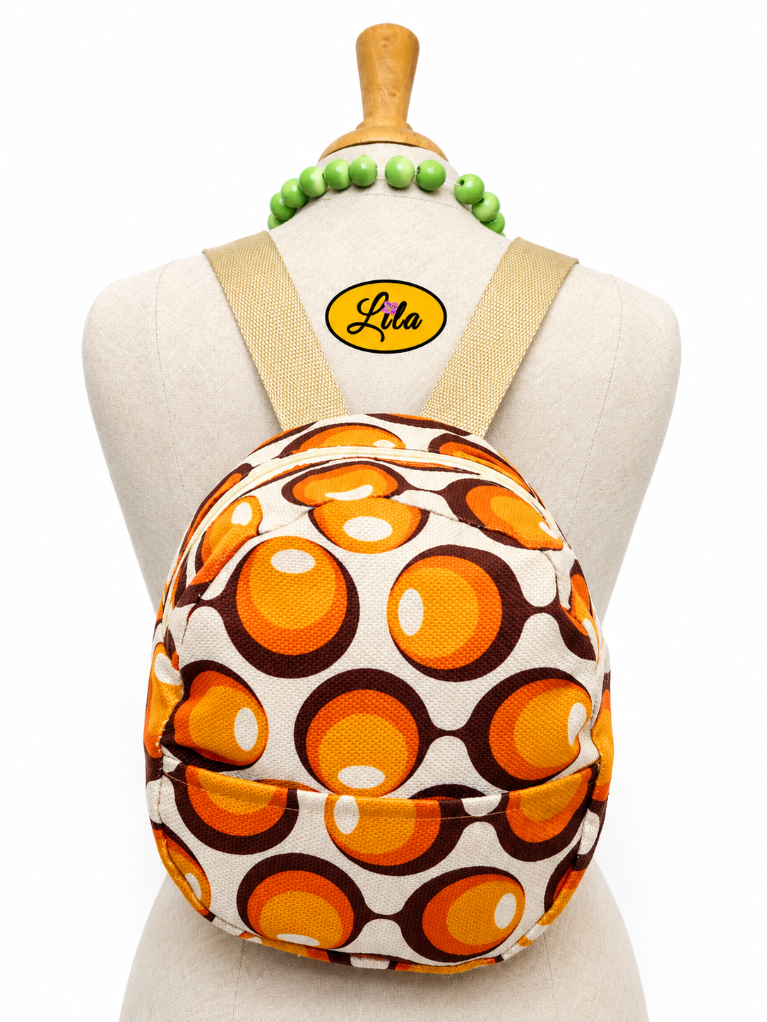 Mini sac à dos en tissu vintage à ronds orange avec poche avant et sangle sable porté sur mannequin de couture sur fond blanc style rétro et tendance