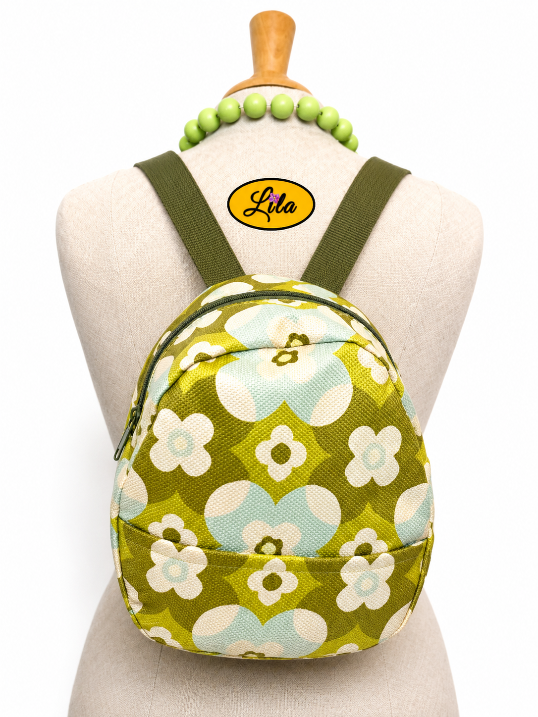 Mini sac à dos en tissu vintage vert fleuri avec poche avant et sangle kaki porté sur mannequin de couture sur fond blanc style bohème et naturel