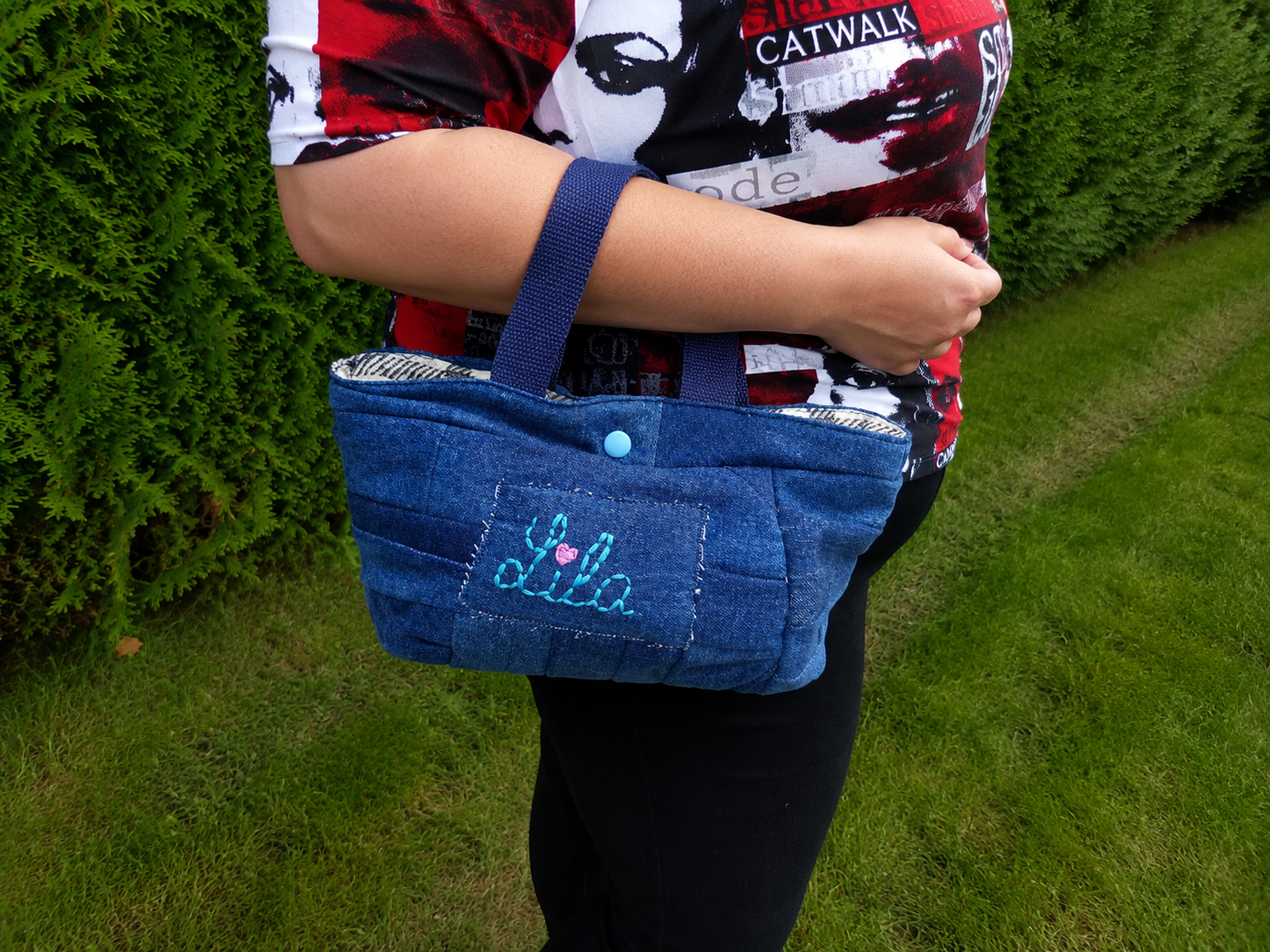 Mini sac à main en jeans recyclé brodé Lila avec cœur rose porté sur l’avant-bras en extérieur photo cadrée sur le sac style artisanal et tendance