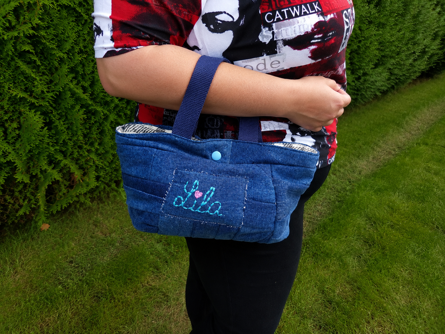 Mini sac à main en jeans recyclé brodé Lila avec cœur rose porté sur l’avant-bras en extérieur photo cadrée sur le sac style artisanal et tendance
