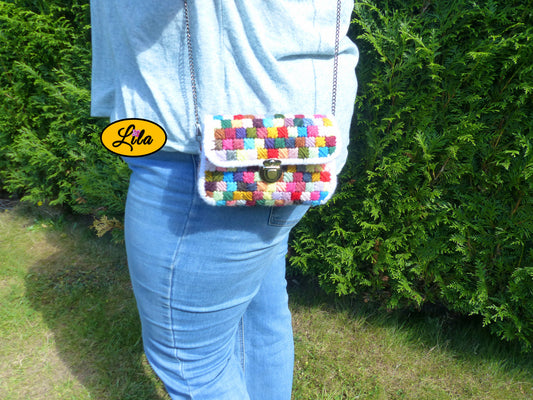 Petit sac à main à carrés multicolores en laine sur canevas rigide porté à l’épaule par un mannequin en extérieur photo cadrée sur le sac style créateur et tendance
