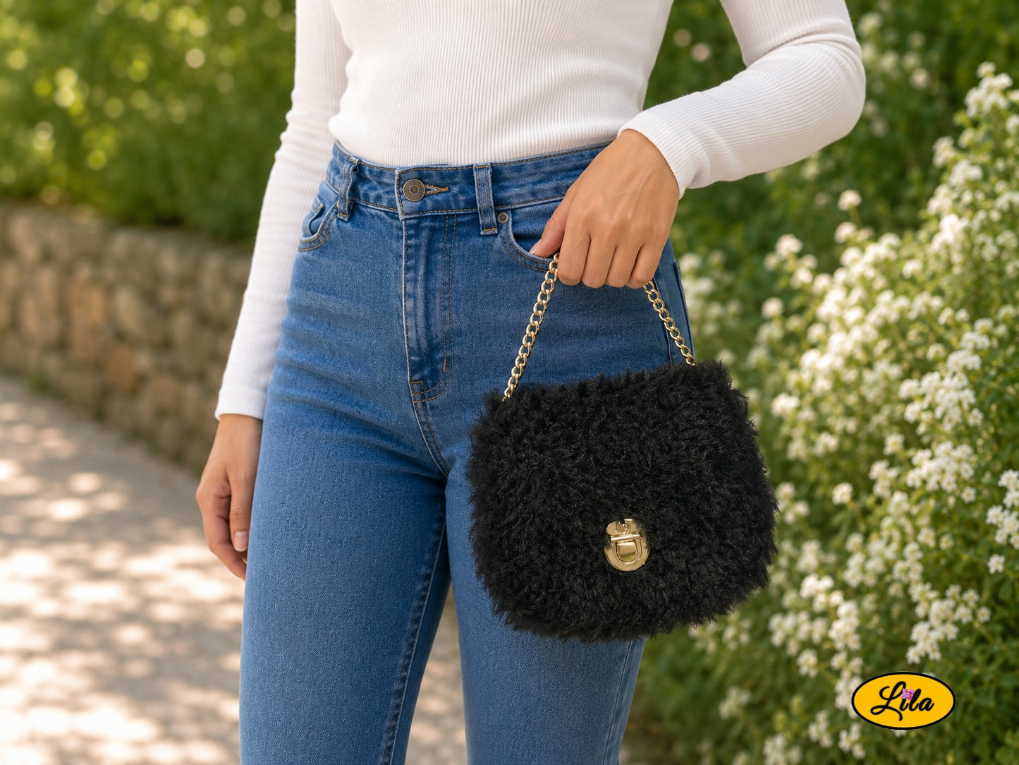 Petit sac à main effet fausse fourrure noire sur canevas rigide porté à la main par un mannequin dans un jardin style chic et tendance