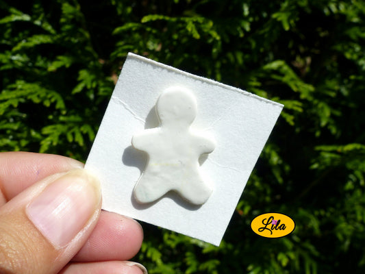 Pin’s bonhomme blanc réalisé en pâte polymère sur carton de présentation blanc photographié devant une haie style kawaii et artisanal