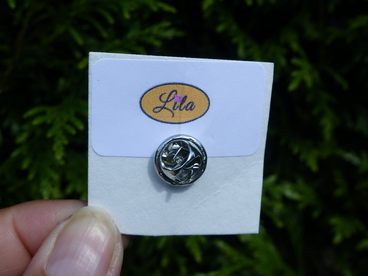 Pin’s bonhomme jaune réalisé en pâte polymère avec attache argentée sur carton de présentation blanc photographié devant une haie style kawaii et artisanal