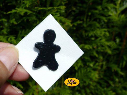 Pin’s bonhomme noir réalisé en pâte polymère sur carton de présentation blanc photographié devant une haie style kawaii et artisanal