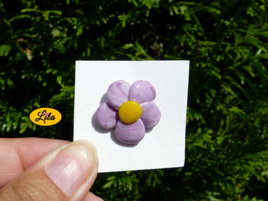 Pin’s fleur aux pétales mauves dégradés réalisé en pâte polymère sur carton de présentation blanc photographié devant une haie style floral et artisanal