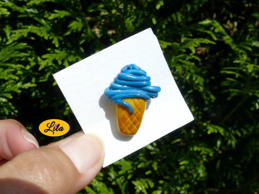 Pin’s cornet de glace italienne bleue réalisé en pâte polymère sur carton de présentation blanc photographié devant une haie style gourmand et kawaii