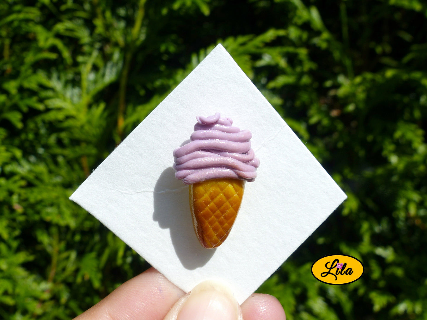 Pin’s cornet de glace italienne mauve dégradée réalisé en pâte polymère sur carton de présentation blanc photographié devant une haie style gourmand et kawaii