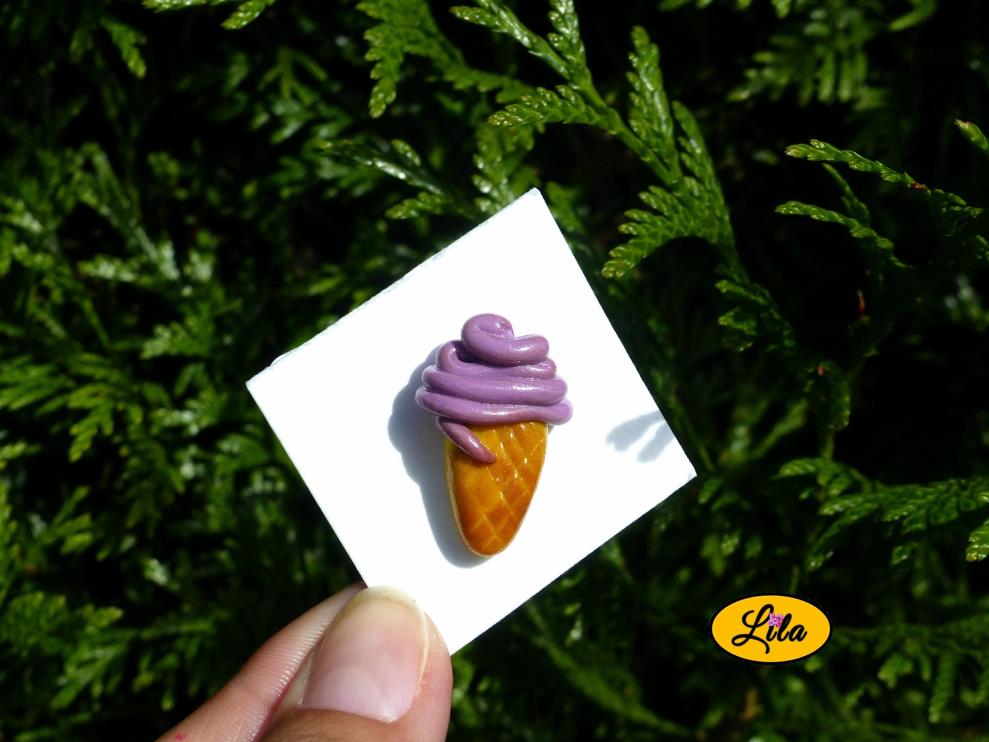 Pin’s glace italienne mauve réalisé en pâte polymère sur carton de présentation blanc photographié devant une haie style gourmand et kawaii