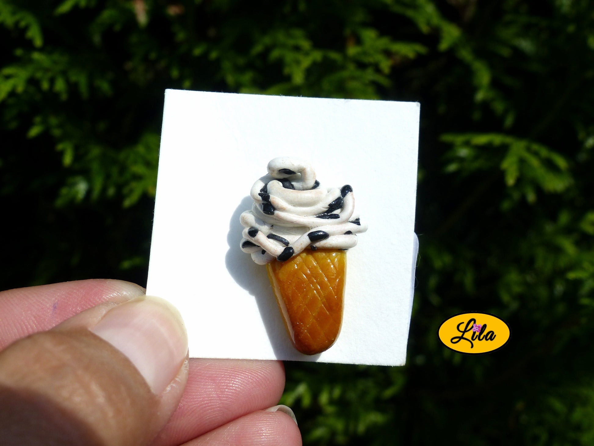 Pin’s glace italienne façon stracciatella réalisé en pâte polymère sur carton de présentation blanc photographié devant une haie style gourmand et kawaii