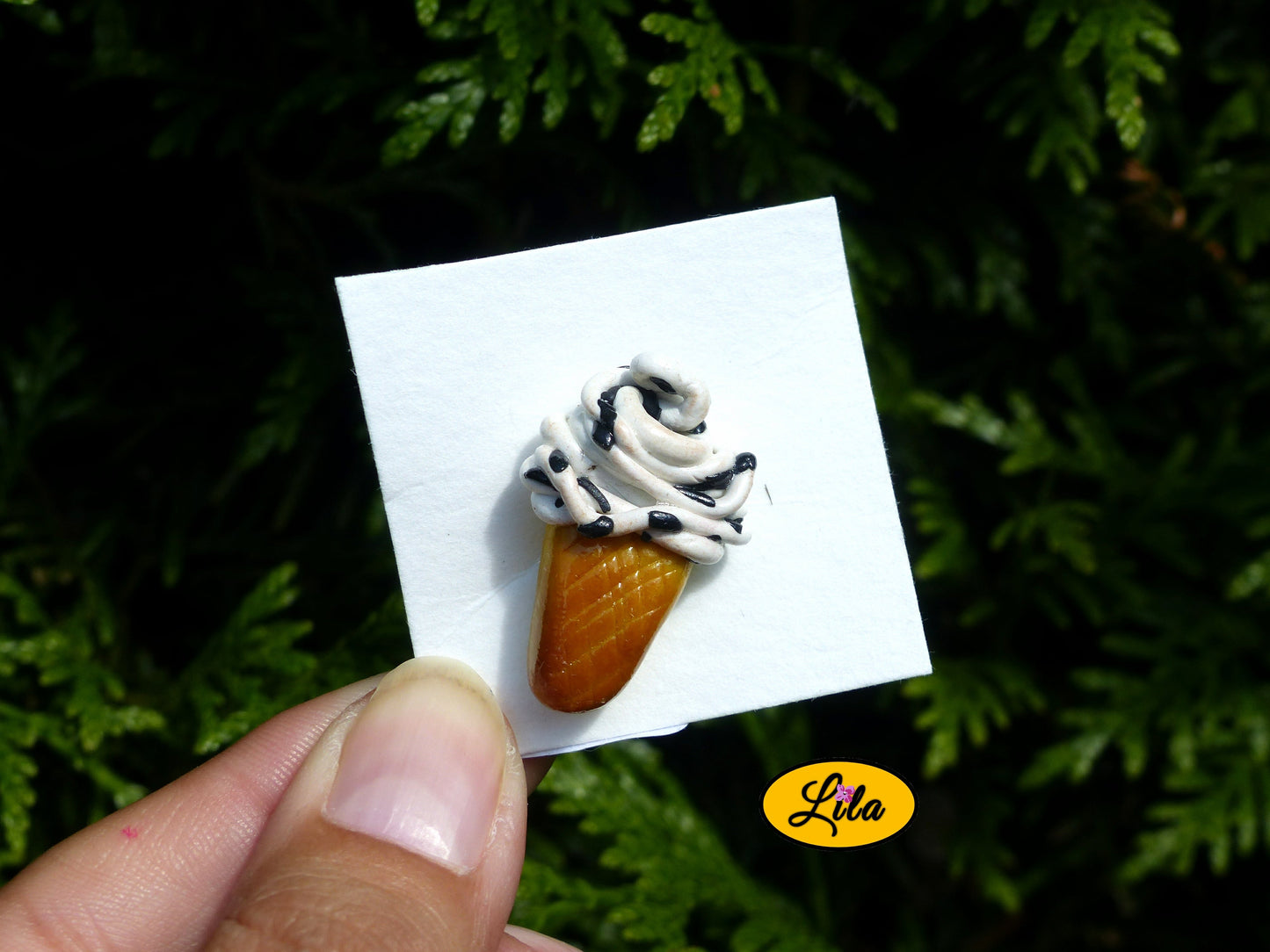 Photo rapprochée d’un pin’s glace italienne façon stracciatella réalisé en pâte polymère sur carton de présentation blanc photographié devant une haie style gourmand et kawaii