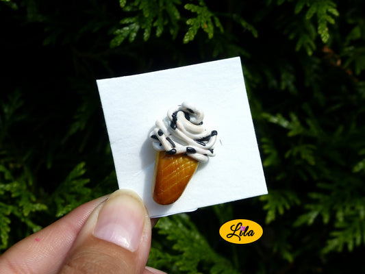 Photo rapprochée d’un pin’s glace italienne façon stracciatella réalisé en pâte polymère sur carton de présentation blanc photographié devant une haie style gourmand et kawaii