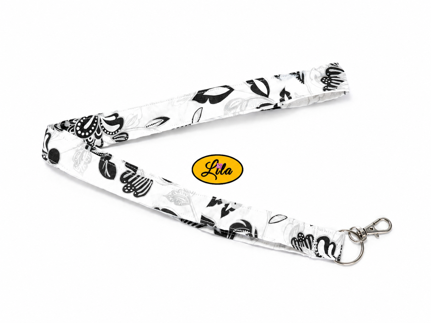 Porte-badge en tissu blanc à motifs noirs baroques légèrement replié en deux sur fond blanc avec mousqueton métallique style rétro et pratique
