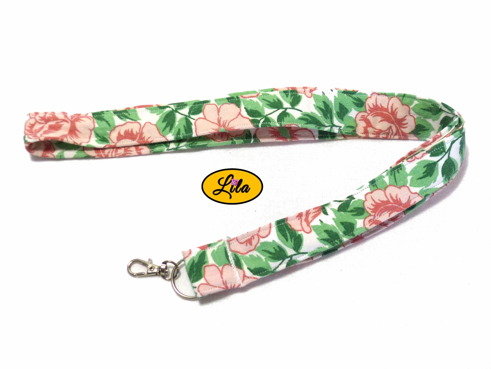 Porte-badge en tissu blanc à motifs fleurs roses vintage et feuilles vertes légèrement replié en deux sur fond blanc avec mousqueton métallique style féminin et pratique