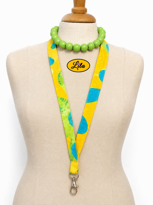 Porte-badge en tissu jaune à motifs floraux bleus porté sur mannequin de couture sur fond blanc avec mousqueton style bohème et artisanal