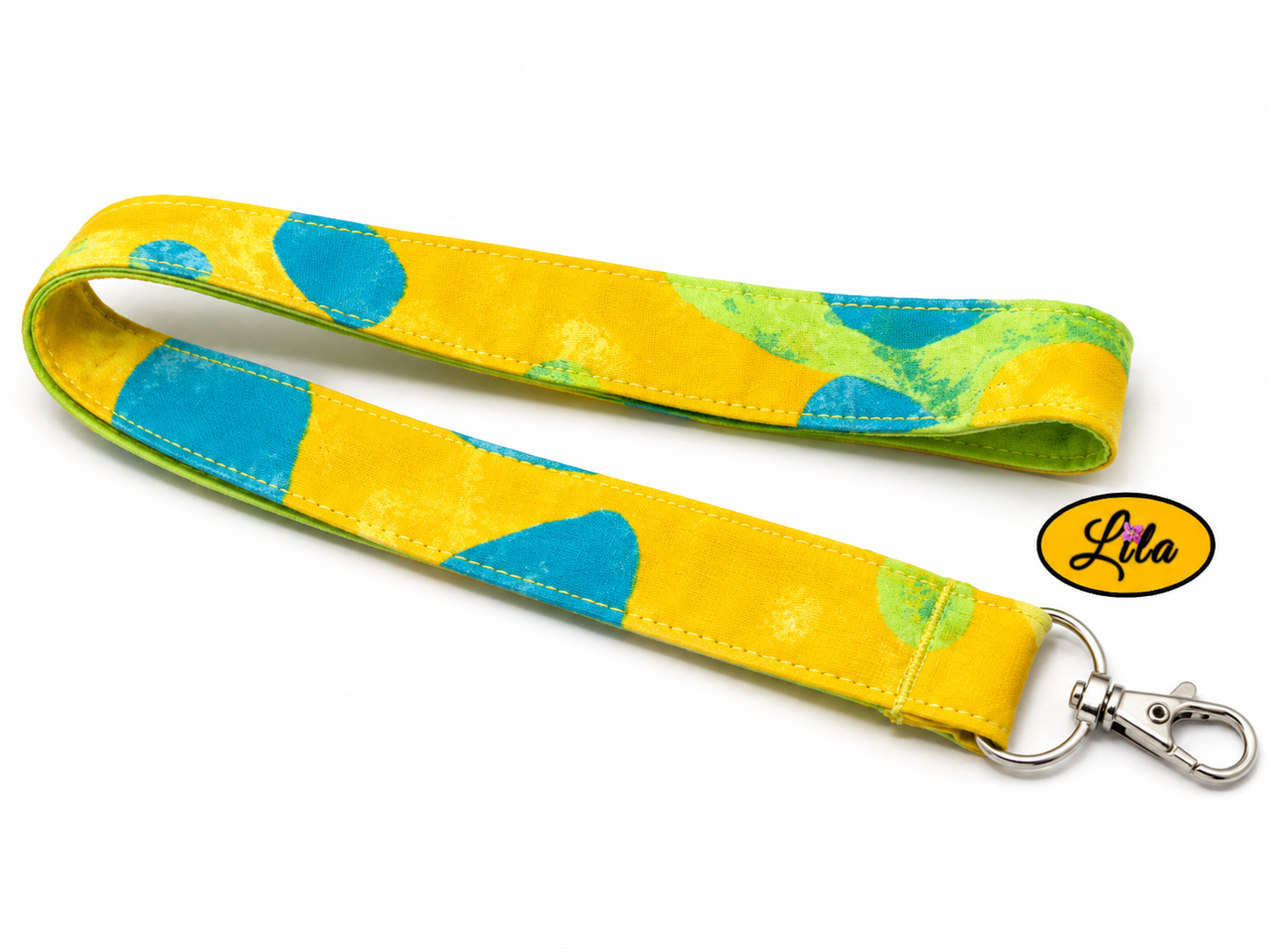 Porte-badge en tissu jaune à motifs fleurs bleues légèrement replié en deux sur fond blanc avec mousqueton métallique style féminin et pratique
