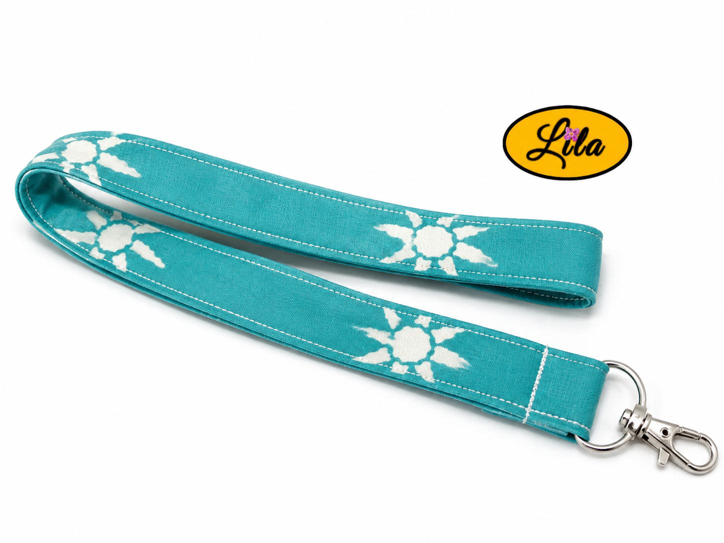 Porte-badge en tissu vert à petits motifs soleils blancs légèrement replié en deux sur fond blanc avec mousqueton métallique style pratique et tendance