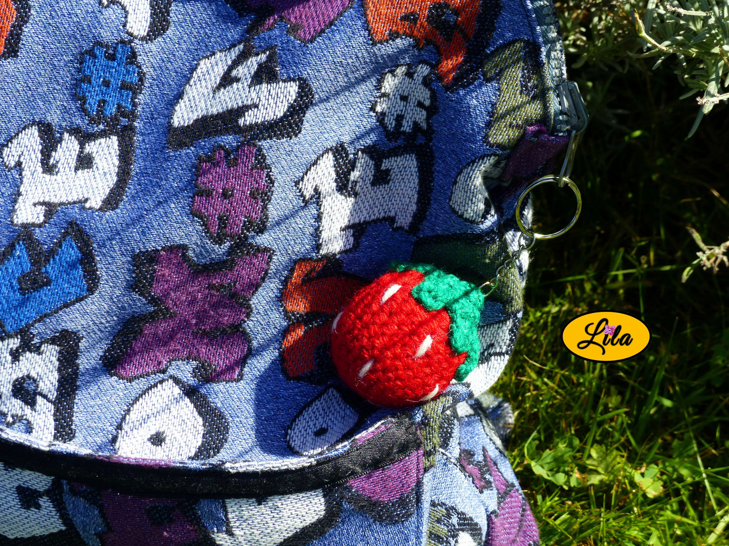 Photo rapprochée d’un porte-clé fraise amigurumi accroché à un sac à dos sur une pelouse style kawaii et artisanal