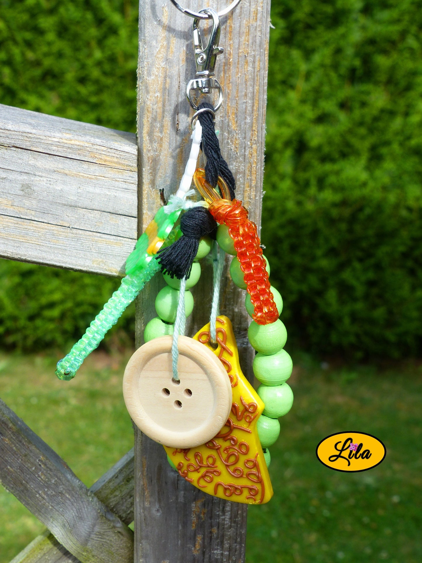 Porte-clés lune dorée esprit nature composé d’une sucette verte en perles à repasser avec bâtonnet blanc, lune jaune ornée de motifs bruns en pâte polymère, bracelet en grosses perles vertes, scoubidous colorés, bouton en bois et bouts de laine tressée suspendus à un mousqueton style bohème et artisanal