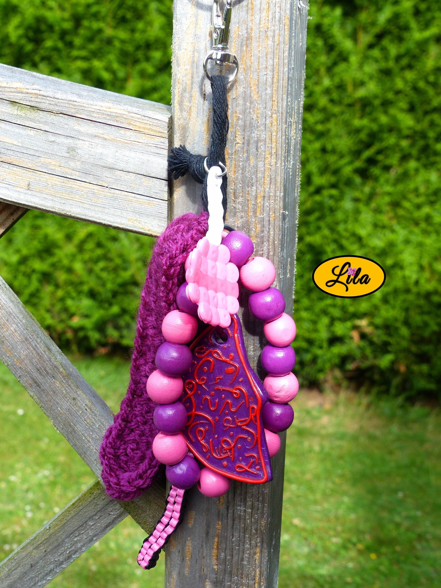 Porte-clés mauve douceur sucrée composé d’une sucette rose en perles à repasser avec bâtonnet blanc, lune mauve ornée de motifs roses en pâte polymère, bracelet en grosses perles mauves et roses, scoubidou noir et rose, languette crochetée mauve et bouts de laine tressée suspendus à un mousqueton style kawaii et artisanal