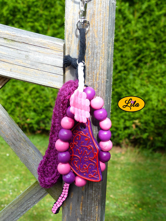 Porte-clés mauve douceur sucrée composé d’une sucette rose en perles à repasser avec bâtonnet blanc, lune mauve ornée de motifs roses en pâte polymère, bracelet en grosses perles mauves et roses, scoubidou noir et rose, languette crochetée mauve et bouts de laine tressée suspendus à un mousqueton style kawaii et artisanal
