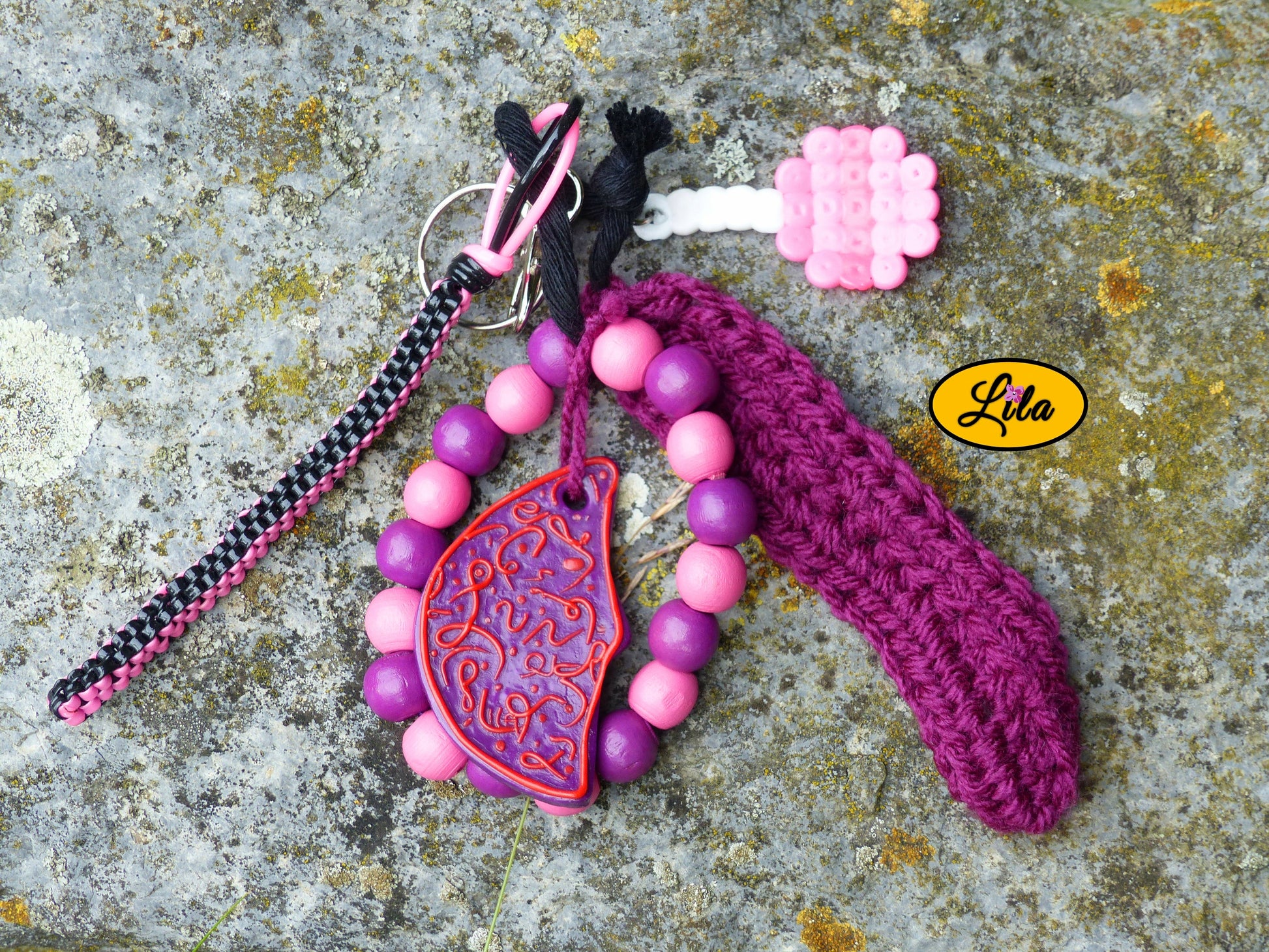Porte-clés mauve douceur sucrée posé sur une pierre vue de haut avec sucette rose en perles à repasser, lune mauve en pâte polymère, grosses perles mauves et roses, languette crochetée et scoubidou noir et rose visibles côte à côte style créatif et bohème