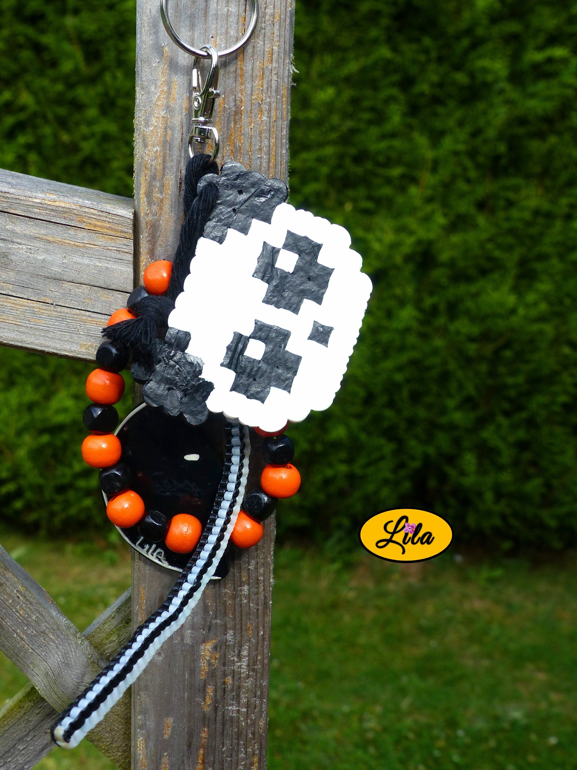 Porte-clés Panda vintage composé d’une tête de panda en perles à repasser, lune noire décorée de motifs blancs en pâte polymère, bracelet de grosses perles noires et orange, scoubidou noir et blanc et bouts de laine tressée suspendus à un mousqueton style kawaii et artisanal