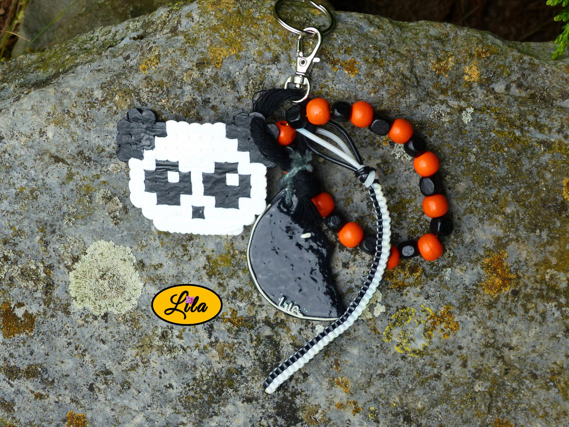 Porte-clés Panda vintage posé sur une pierre vue de haut avec tête de panda en perles à repasser, lune noire en pâte polymère, grosses perles noires et orange et scoubidou noir et blanc visibles côte à côte style créatif et récup