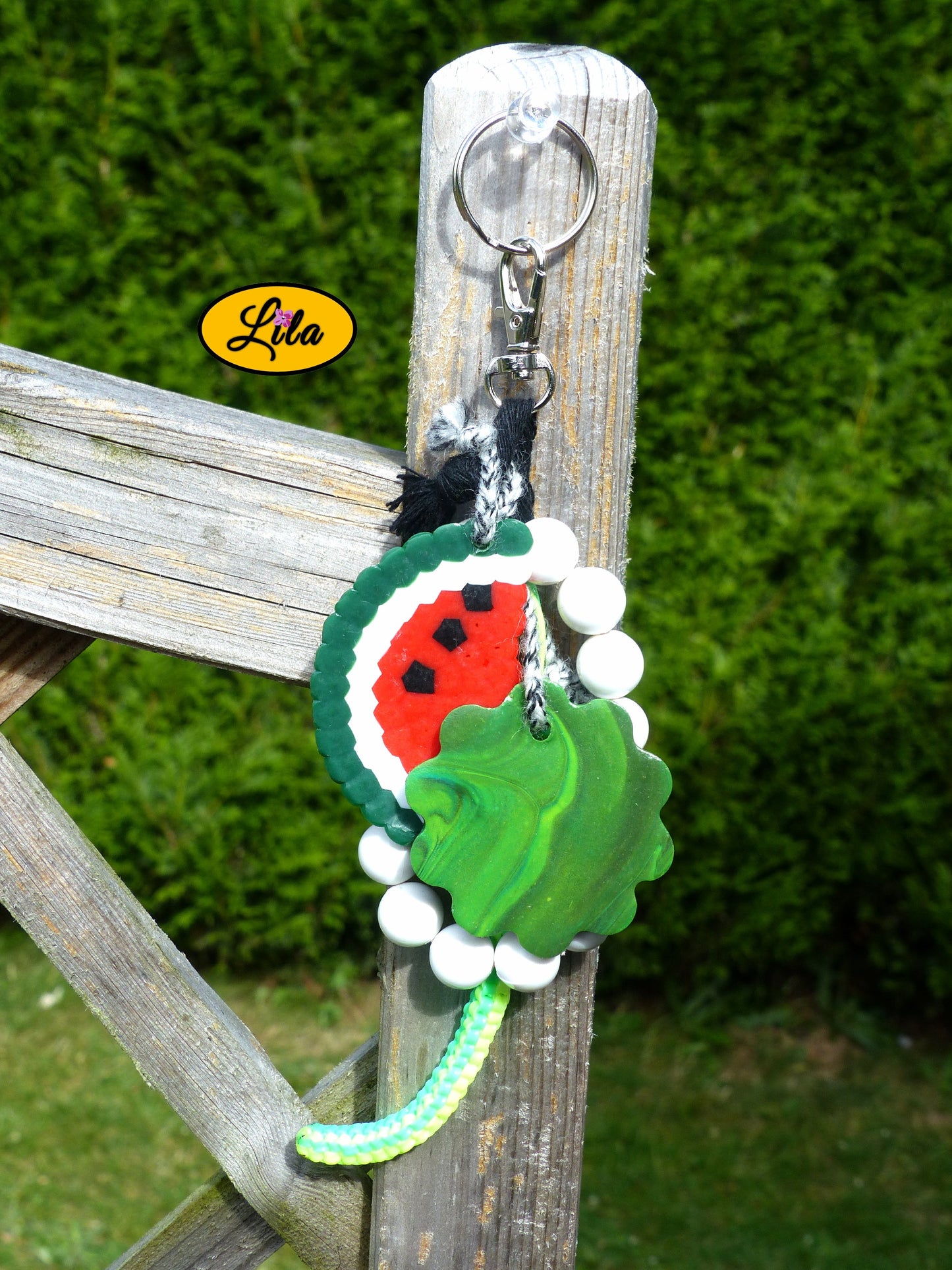 Porte-clés pastèque et perles composé d’une demi-tranche de pastèque en perles à repasser, fleur en pâte polymère dans les tons de vert dégradé, bracelet en grosses perles blanches, scoubidou et bouts de laine tressée suspendus à un mousqueton style kawaii et artisanal