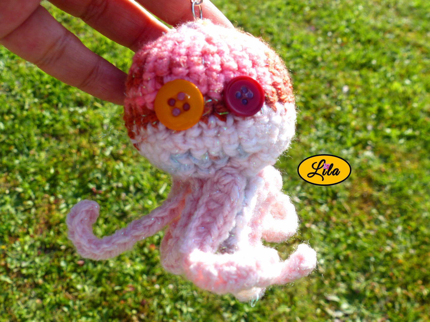 Porte-clé Poulpy pieuvre amigurumi rose aux tons dégradés pailletés réalisée au crochet avec yeux en boutons orange et fuchsia tenu dans une main en extérieur dans un jardin style handmade et mignon