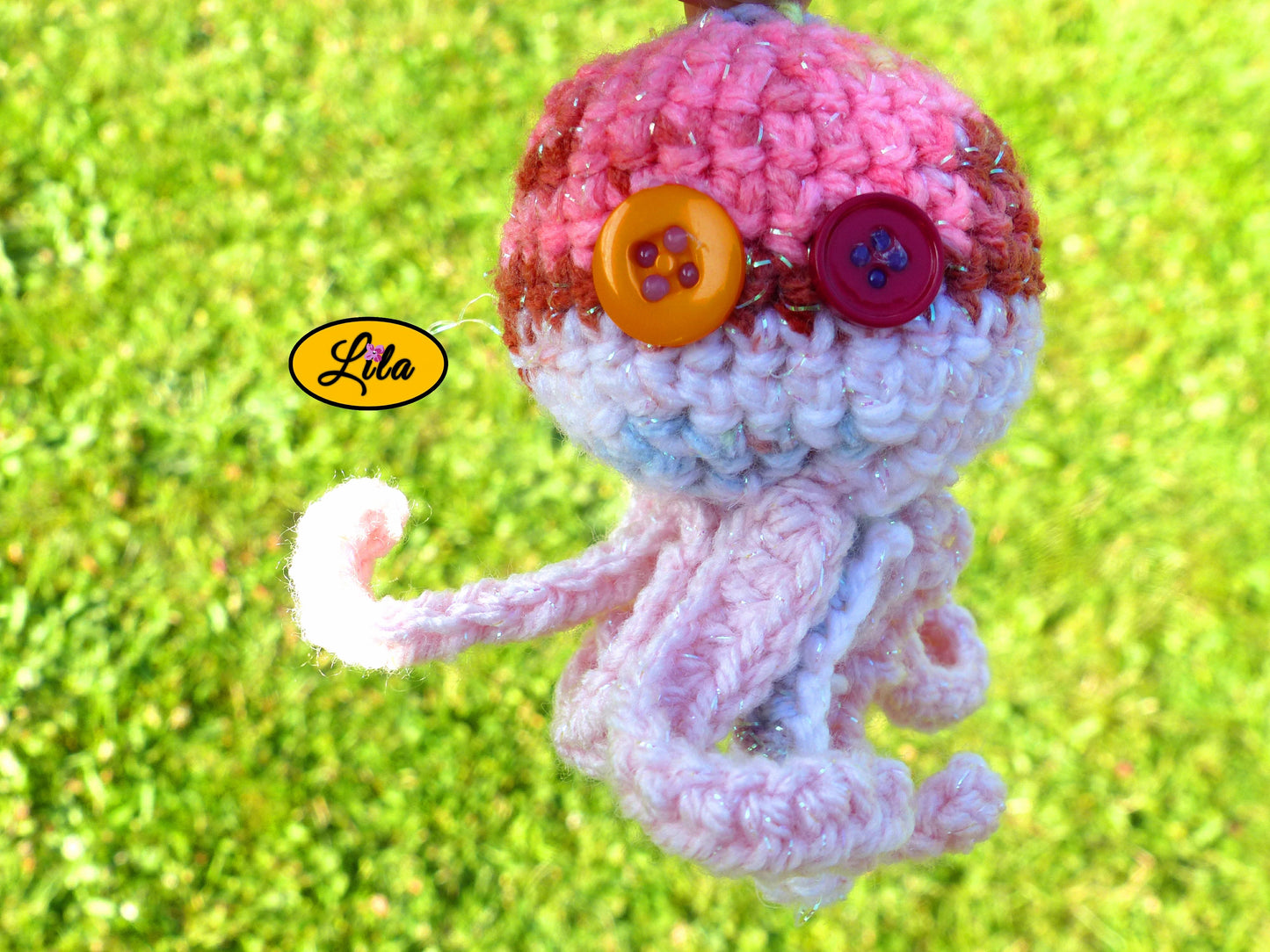 Photo rapprochée du porte-clé Poulpy pieuvre amigurumi rose dégradé pailleté au crochet avec yeux en boutons orange et fuchsia dans un jardin style artisanal et féerique