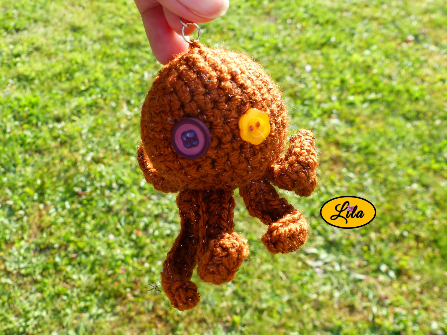 Porte-clé Poulpy pieuvre amigurumi brune pailletée réalisée au crochet avec yeux en boutons fleur jaune et mauve foncé tenu dans une main en extérieur dans un jardin style handmade et chaleureux