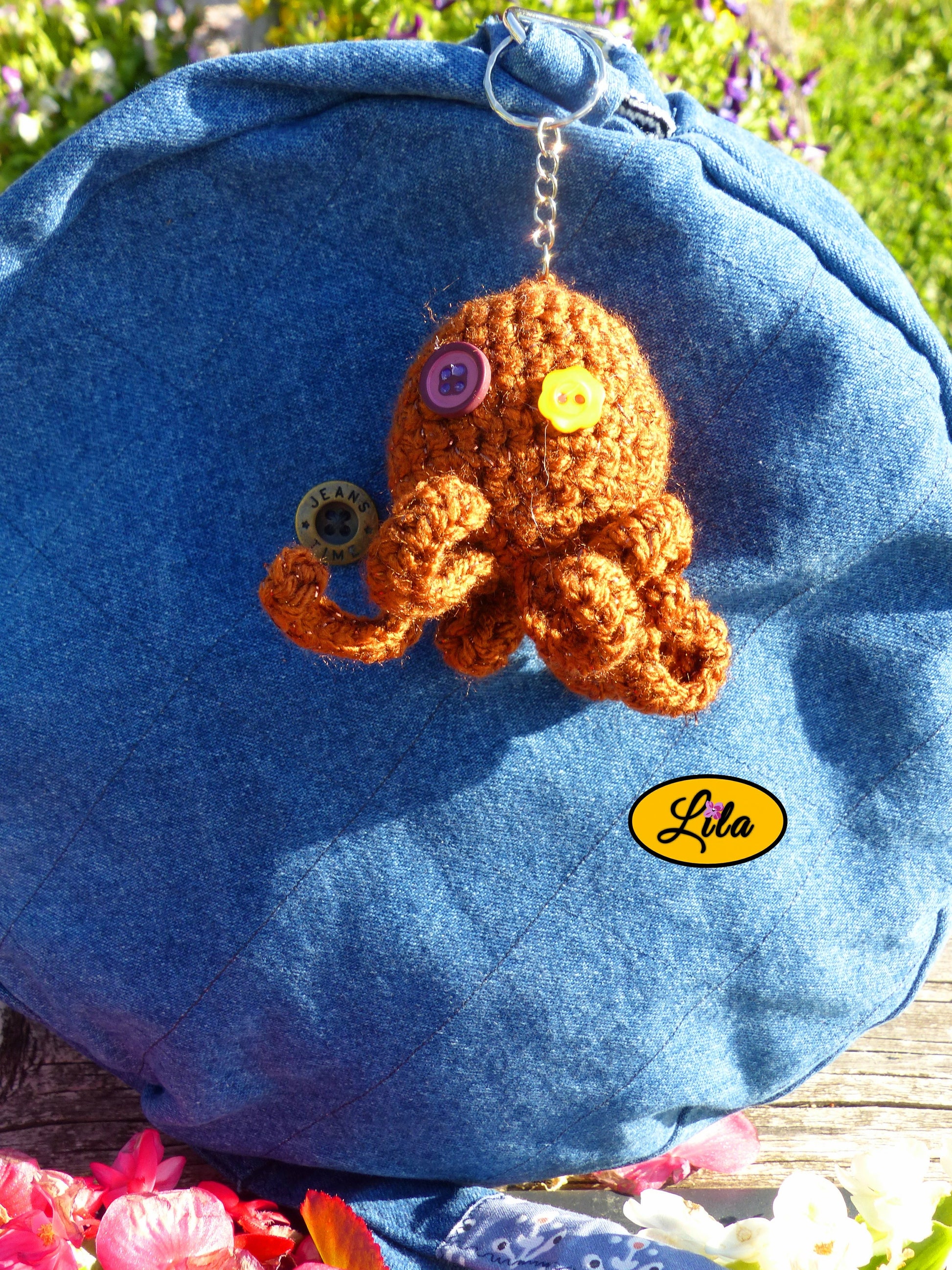 Porte-clé Poulpy pieuvre amigurumi brune pailletée réalisée au crochet avec yeux en boutons fleur jaune et mauve foncé accroché à un sac style bohème et artisanal