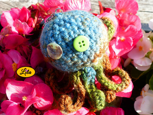 Porte-clé Poulpy pieuvre amigurumi chamarrée aux tons vert bleu et brun réalisée au crochet avec yeux en boutons vert et multicolore posé sur un lit de fleurs style bohème et automnal