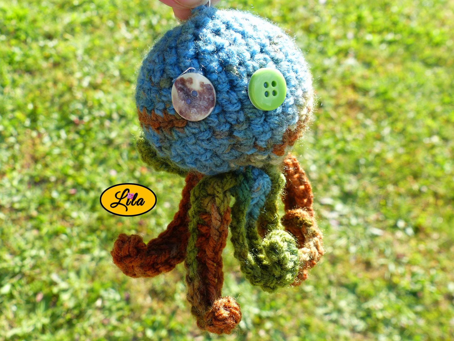 Photo rapprochée du porte-clé Poulpy pieuvre amigurumi chamarrée au crochet dans des tons automnaux vert bleu et brun avec yeux en boutons vert et multicolore style artisanal et kawaii