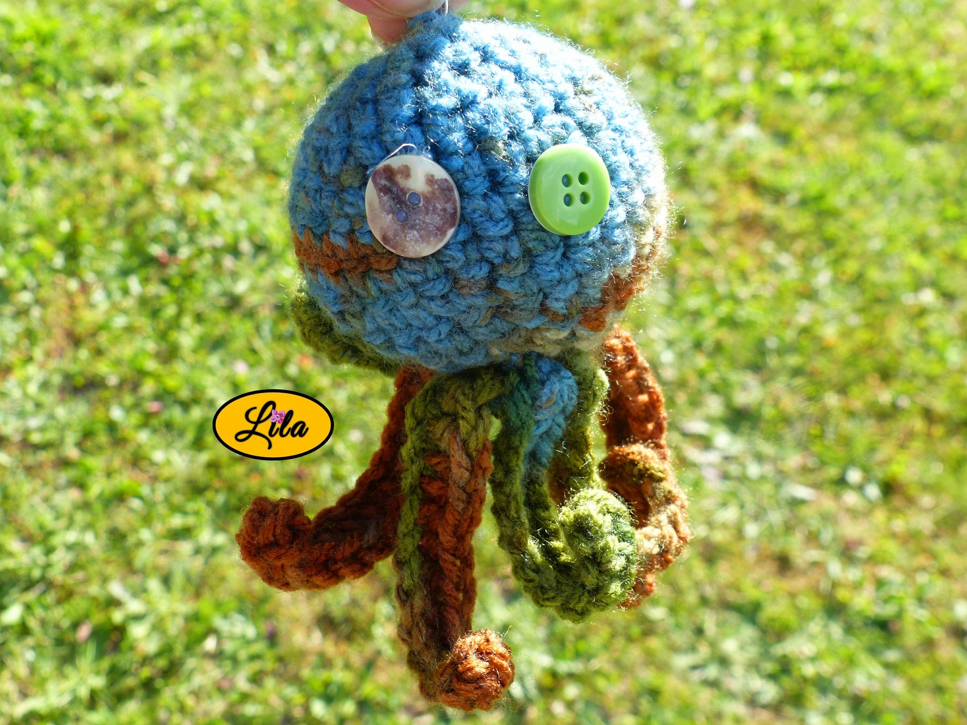 Photo rapprochée du porte-clé Poulpy pieuvre amigurumi chamarrée au crochet dans des tons automnaux vert bleu et brun avec yeux en boutons vert et multicolore style artisanal et kawaii
