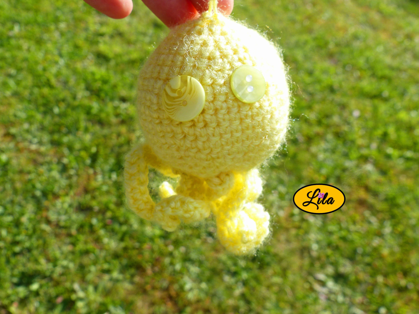Porte-clé Poulpy pieuvre amigurumi jaune réalisée au crochet avec yeux en boutons jaunes de différentes nuances tenu dans une main en extérieur dans un jardin style handmade et mignon