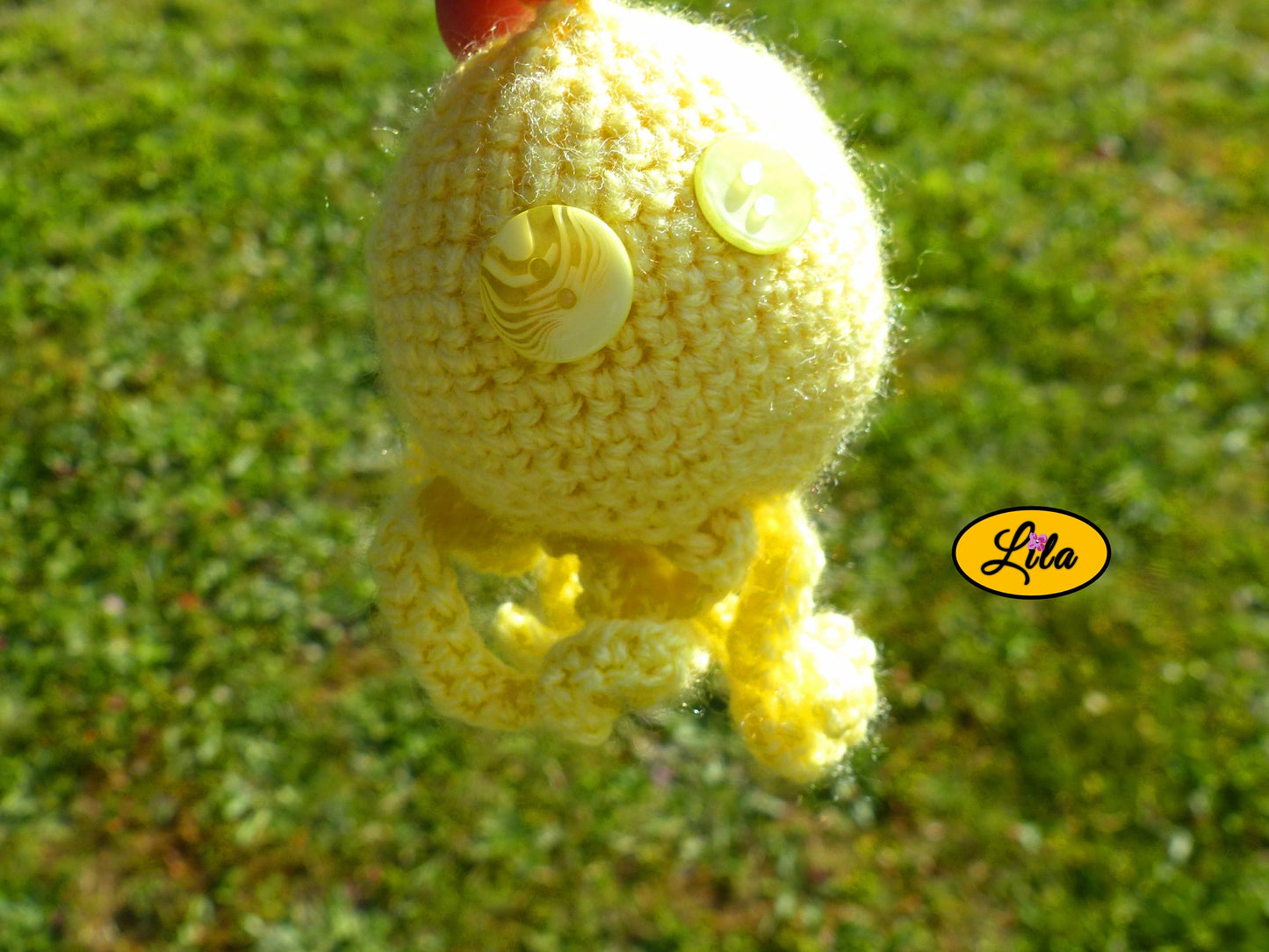 Photo rapprochée du porte-clé Poulpy pieuvre amigurumi jaune au crochet avec yeux en boutons jaunes de différentes teintes dans un jardin style artisanal et kawaii