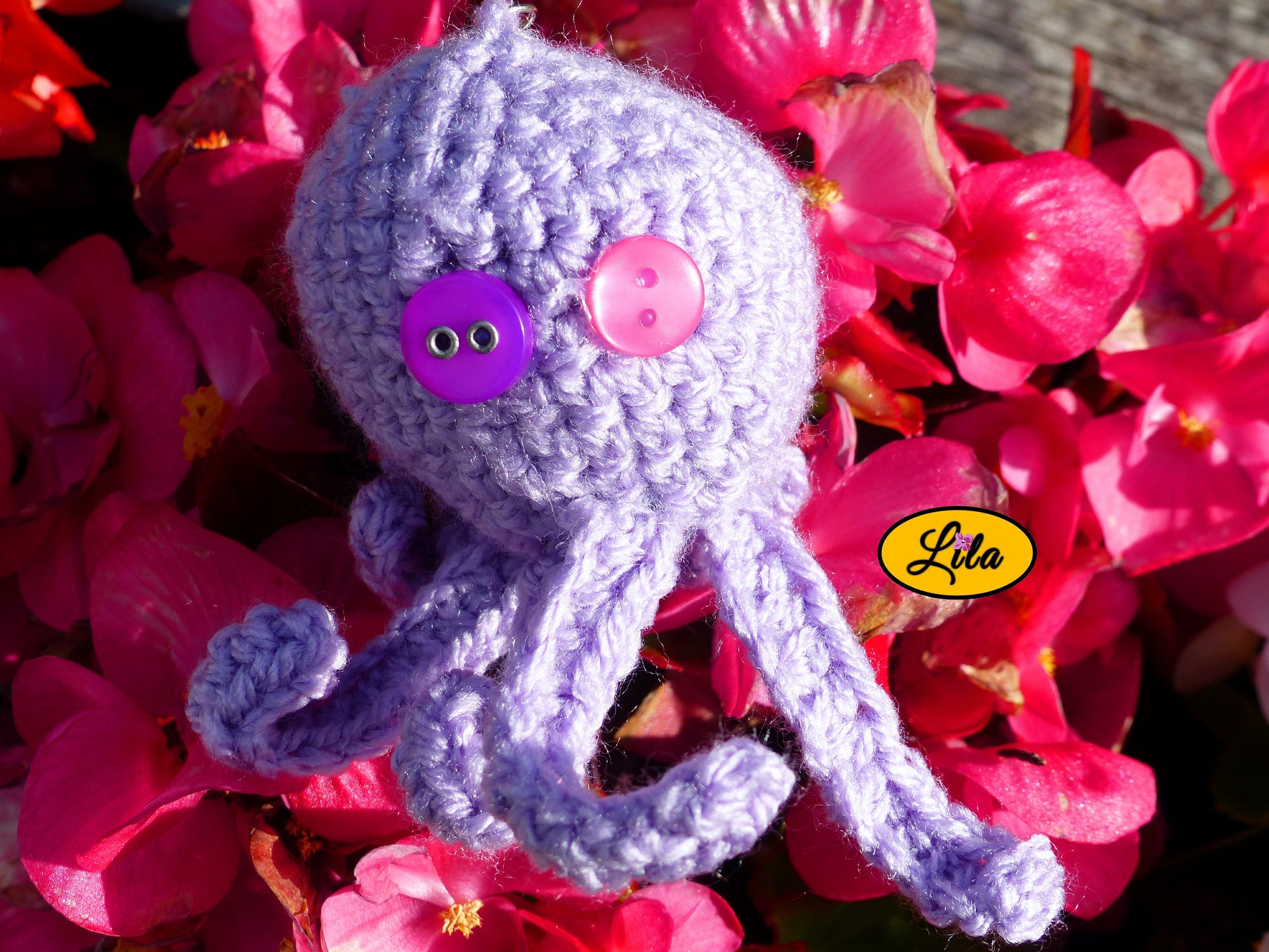 Porte-clé Poulpy pieuvre amigurumi mauve clair réalisée au crochet avec yeux en boutons mauve et rose posé sur un lit de fleurs style kawaii et artisanal