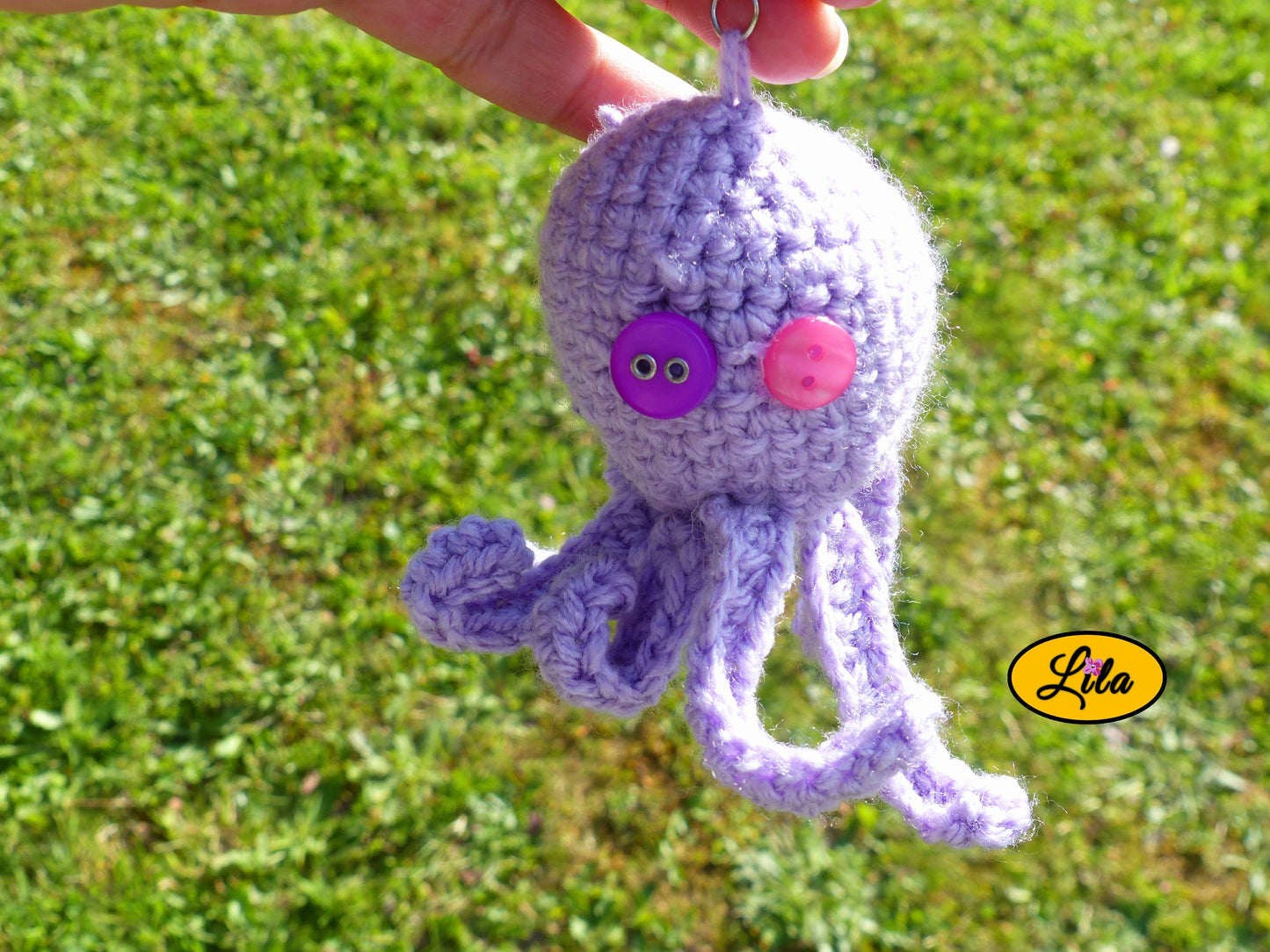 Porte-clé Poulpy pieuvre amigurumi mauve clair réalisée au crochet avec yeux en boutons mauve et rose tenu dans une main en extérieur dans un jardin style handmade et mignon