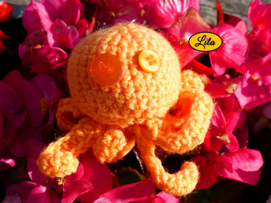 Porte-clé Poulpy pieuvre amigurumi orange réalisée au crochet avec yeux en boutons orange posé sur un lit de fleurs style kawaii et artisanal