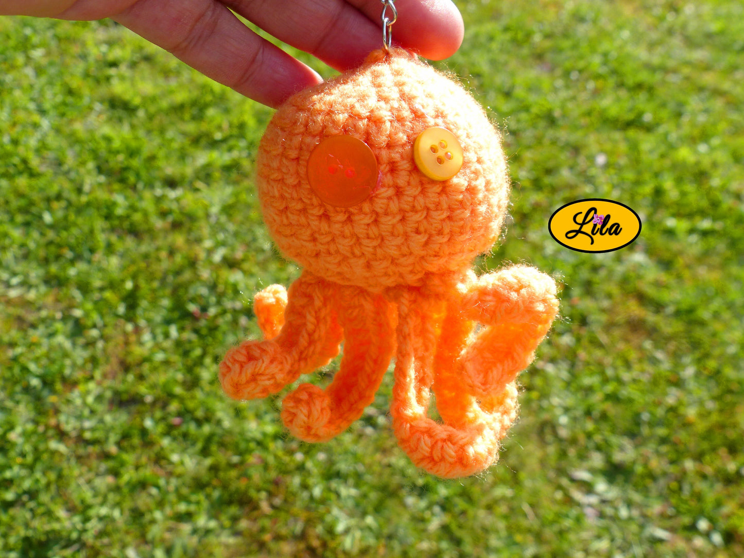 Porte-clé Poulpy pieuvre amigurumi orange réalisée au crochet avec yeux en boutons orange tenu dans une main en extérieur dans un jardin style handmade et mignon