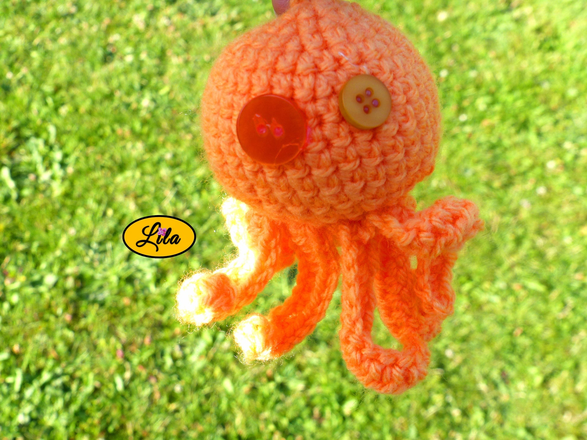 Photo rapprochée du porte-clé Poulpy pieuvre amigurumi orange au crochet avec yeux en boutons orange dans un jardin style artisanal et kawaii